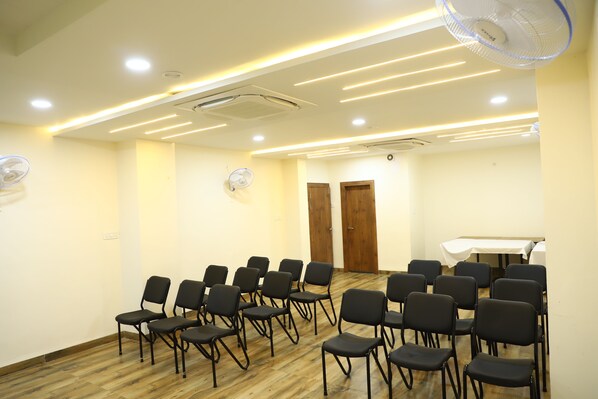 Uma sala de conferências com fileiras de cadeiras, uma mesa e ventiladores no teto.