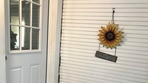 A clean, well-maintained entryway with a white door, a welcome sign, a sun decoration, a black trash bin, a white laundry basket, and a doormat with a vintage design. - Historic home 2-bedroom upstairs pet friendly apartment w/ pool in St. Aug  (St. Augustine)