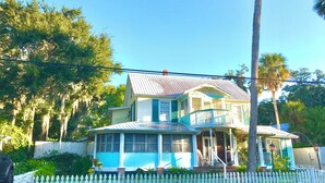 A two-story house with a blue and white exterior, a porch with a railing, and a white picket fence. - Historic home 2-bedroom upstairs pet friendly apartment w/ pool in St. Aug  (St. Augustine)