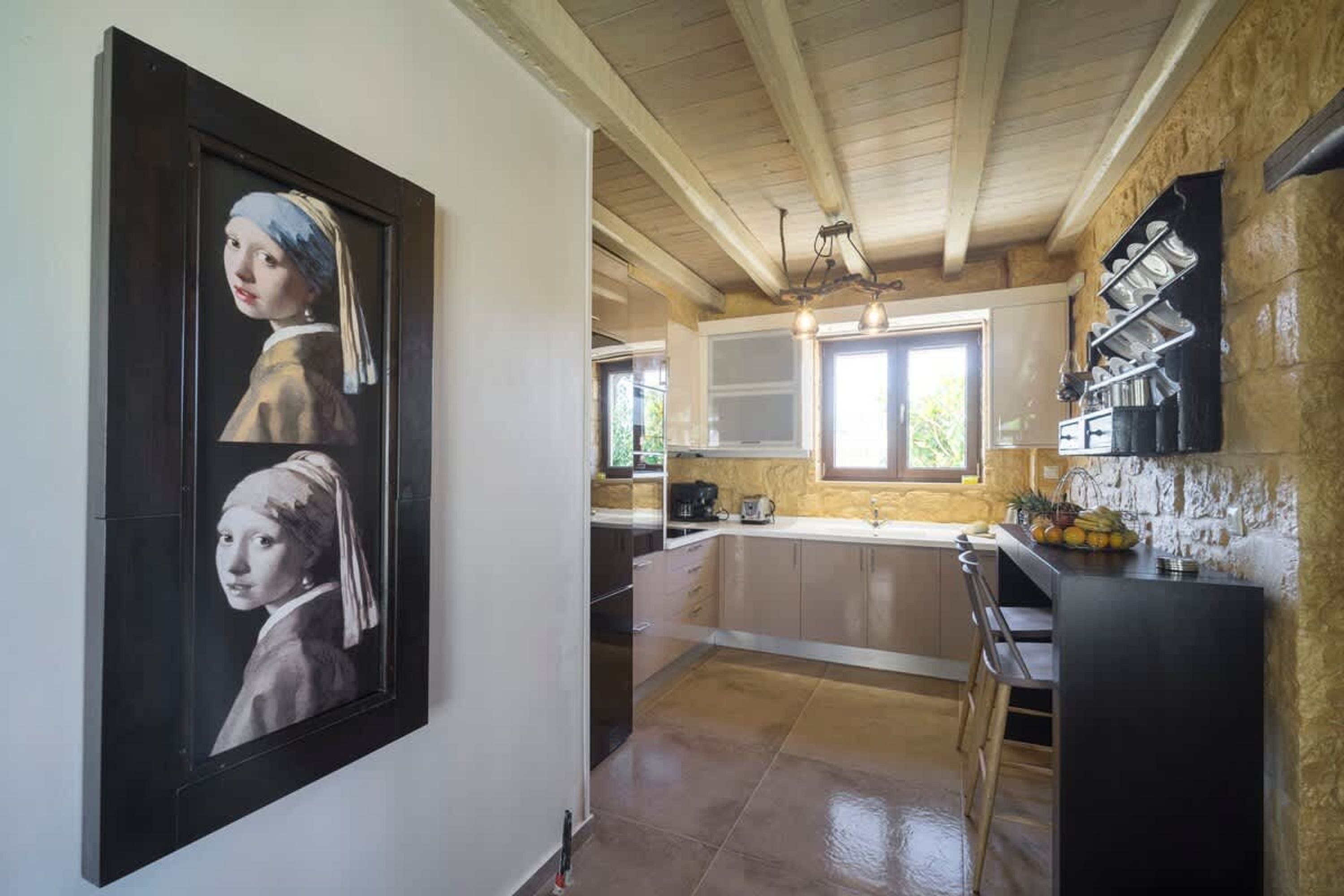A kitchen with a large painting, wooden ceiling beams, and a stone wall.