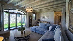 A spacious living room with a large sectional sofa, a round coffee table, and a dining area with a wooden table and chairs. - Heraklion Twins House - Private Pool Retreat (Hersonissos)