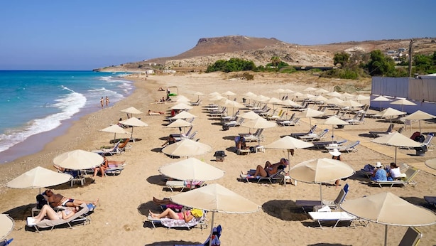 A beach with numerous sun loungers and umbrellas, a clear sky, and a rocky landscape in the background. - Heraklion Twins House - Private Pool Retreat (Hersonissos)