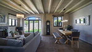 A spacious living room with a large sofa, a dining table with chairs, a fireplace, and a large mirror on the wall. - Heraklion Twins House - Private Pool Retreat (Hersonissos)