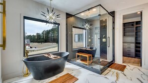 Un baño moderno con una bañera independiente, cabina de ducha con mampara de vidrio y un amplio ventanal con vistas al exterior.