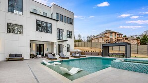 Una casa moderna de dos pisos con piscina, mobiliario exterior y un muro de piedra.