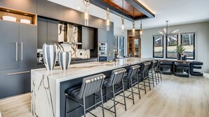 Una cocina moderna con una isla de mármol, taburetes de bar e iluminación colgante.