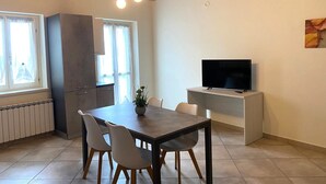 A modern living room with a brick ceiling, a dining table with chairs, a TV on a stand, and a large window with curtains. - Ideal apartment for couple and family in the heart of Monferrato (Castell'Alfero)