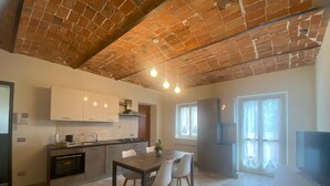 A modern kitchen with a brick ceiling, white cabinets, and a dining area with a table and chairs. - Ideal apartment for couple and family in the heart of Monferrato (Castell'Alfero)