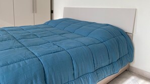 A bed with a blue quilt in a room with white walls and a white headboard. - Ideal apartment for couple and family in the heart of Monferrato (Castell'Alfero)