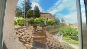 A view through a window with a brick pathway leading to a bench, surrounded by greenery and a building in the background. - Ideal apartment for couple and family in the heart of Monferrato (Castell'Alfero)