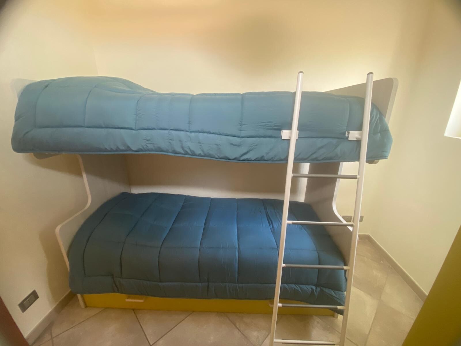 Ein Etagenbett mit einer Leiter, einem gelben Fußteil und einem Fenster im Oberbett.