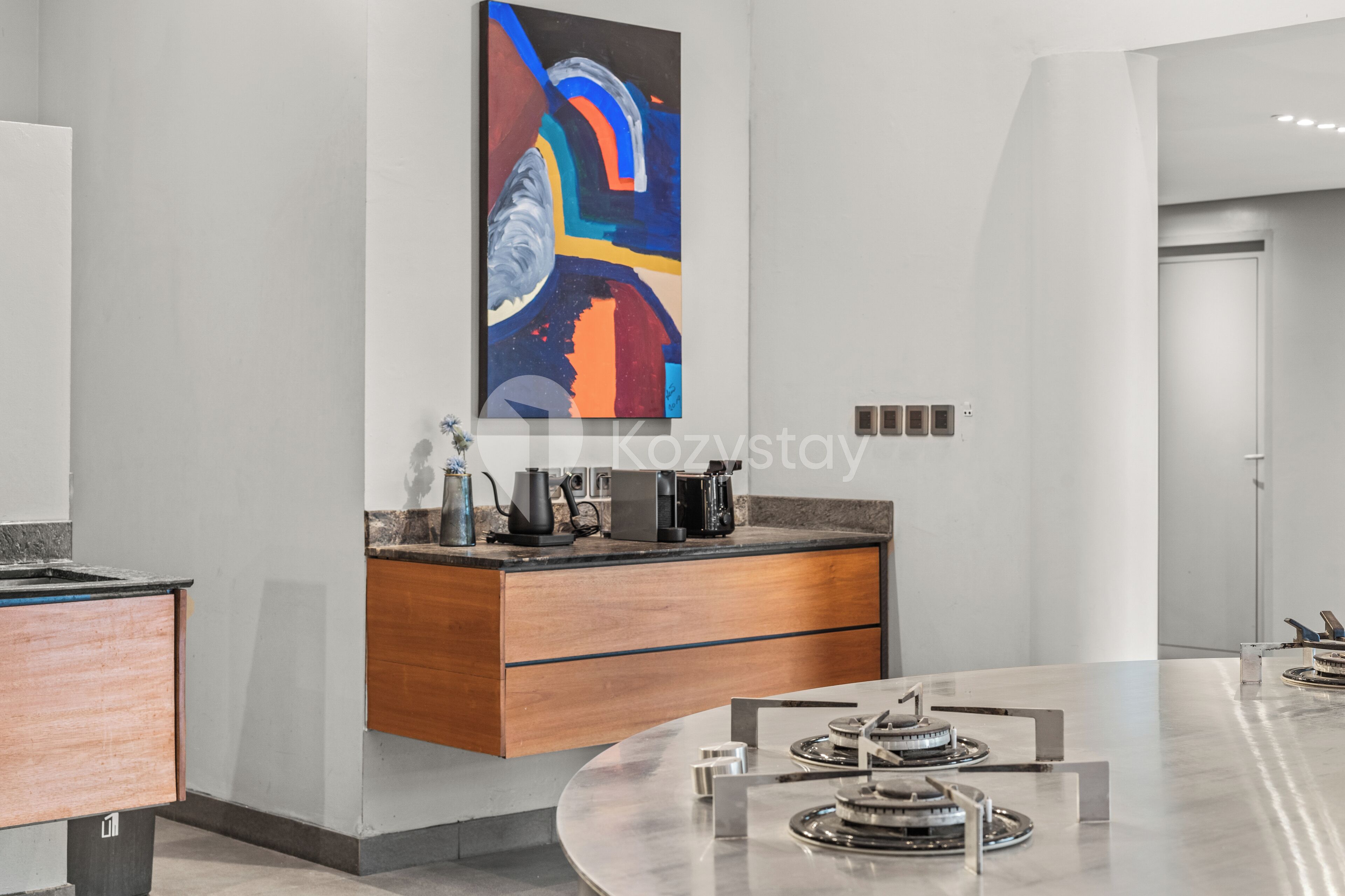 A modern kitchen with a central island, a coffee machine, and a colorful abstract painting on the wall.