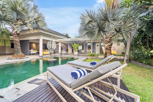 Relax by the serene pool surrounded by lush greenery and lounge chairs.