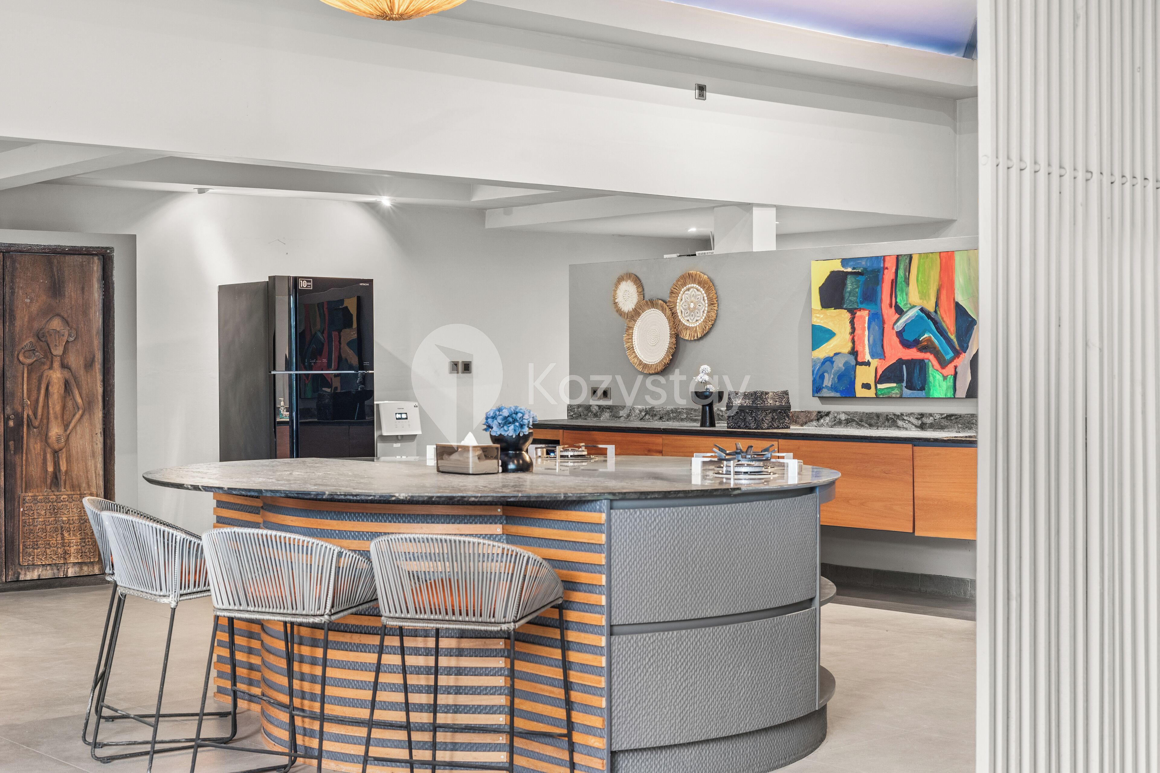 Une cuisine moderne dotée d’un îlot central, de tabourets de bar et d’un tableau abstrait aux couleurs vives.