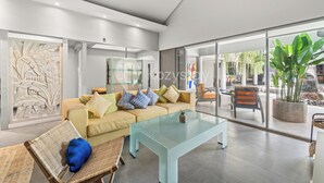 Una sala de estar moderna con una mesa de centro de vidrio, un sofá con cojines estampados y vistas al área exterior a través de grandes puertas de cristal.