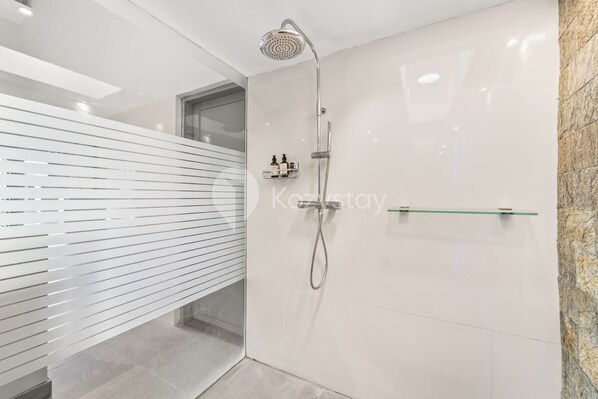 A modern bathroom with a shower, a glass shelf with toiletries, and a stone wall.