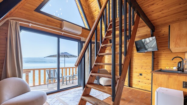 A wooden interior with a staircase, a sofa, a TV, and a view of the sea. - Roseira Bungalov (Milas)