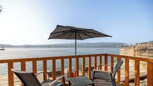 A wooden deck with a table and chairs, overlooking a body of water with distant land. - Roseira Bungalov (Milas)