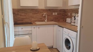 Une cuisine compacte dotée d’un plan de travail en bois, d’un lave-linge encastré et de meubles blancs.