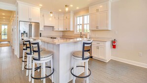 A modern kitchen with white cabinetry, a stainless steel refrigerator, a central island with bar stools, and a window providing natural light.