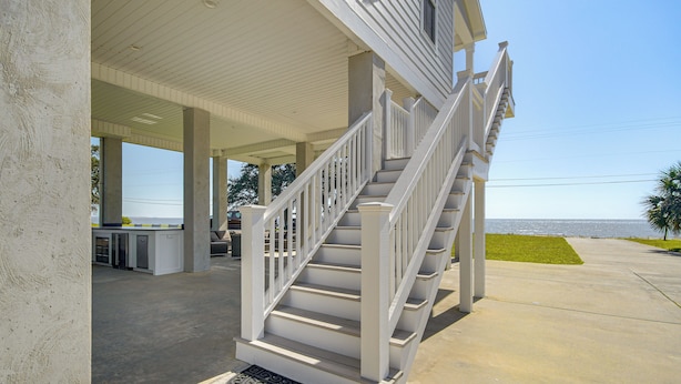 A covered outdoor area with a staircase leading to a second floor, a concrete floor, and a view of the ocean.
