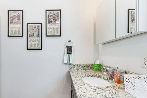 Un bagno con lavabo in granito, un lavandino, uno specchio e quadri appesi al muro.