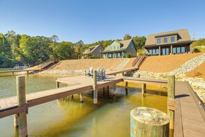 A lakeside property with a wooden dock extending into the water, surrounded by a stone embankment and a forested area. - Waterfront Home in Alex City, Near Auburn (Alexander City)