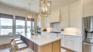 A modern kitchen with a large island, white cabinetry, stainless steel appliances, and a view of a lake. - Waterfront Home in Alex City, Near Auburn (Alexander City)