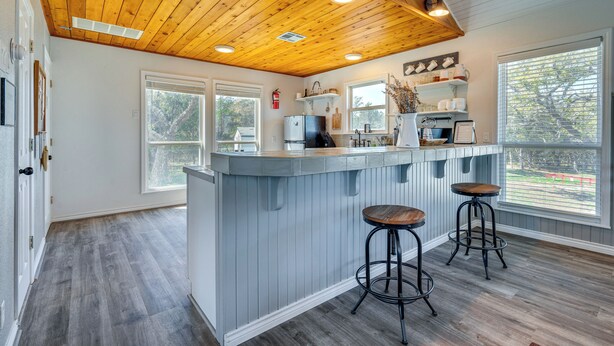 A kitchen with a wooden ceiling, a bar area with stools, and a view through large windows. - Expansive Bertram Retreat w/ Pool, on 28 Acres! (Bertram)