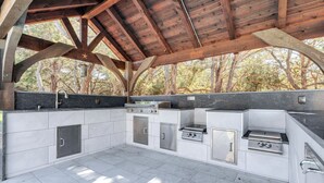 An outdoor kitchen with a stone countertop, stainless steel appliances, and a wooden ceiling. - Expansive Bertram Retreat w/ Pool, on 28 Acres! (Bertram)