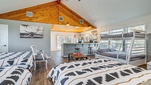 A cozy room with two beds, a wooden ceiling, a dining area, and a view through large windows. - Expansive Bertram Retreat w/ Pool, on 28 Acres! (Bertram)