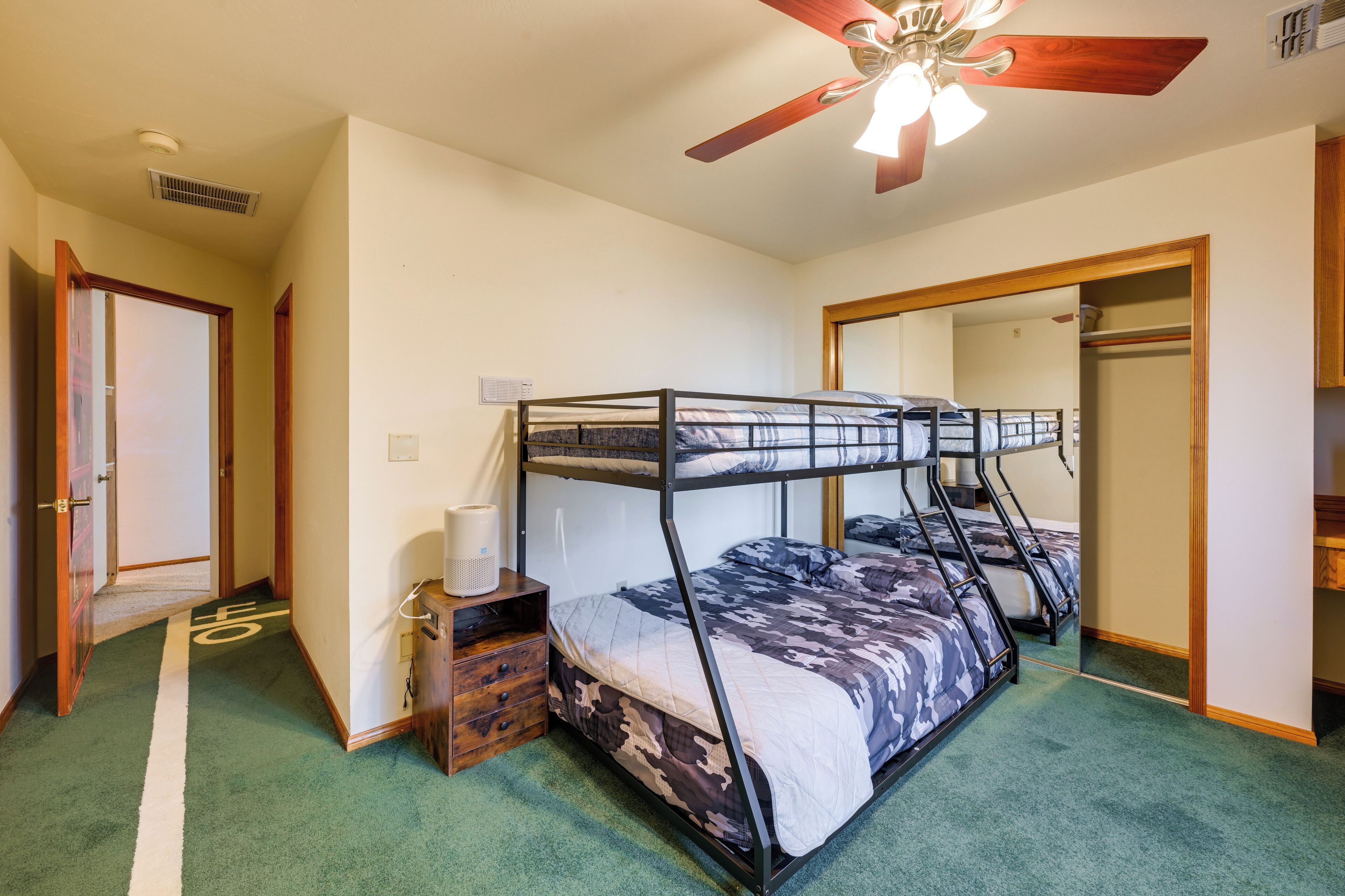 A bunk bed room with a ceiling fan, a mirror, and a wooden dresser.