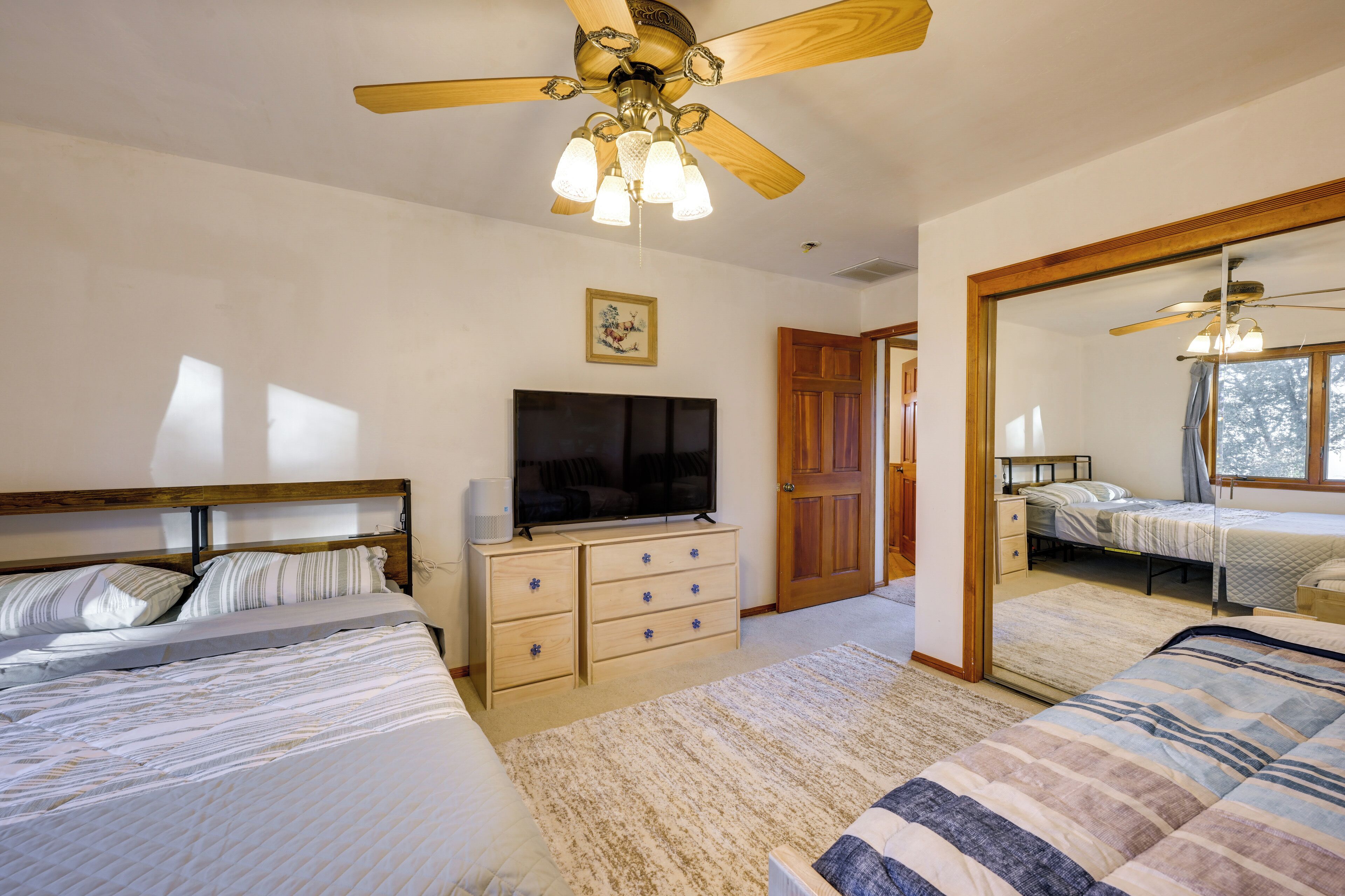 A bedroom with two beds, a ceiling fan, a TV on a wooden dresser, and a door leading to another room.