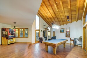 A spacious room with a pool table, wooden flooring, and a large window.
