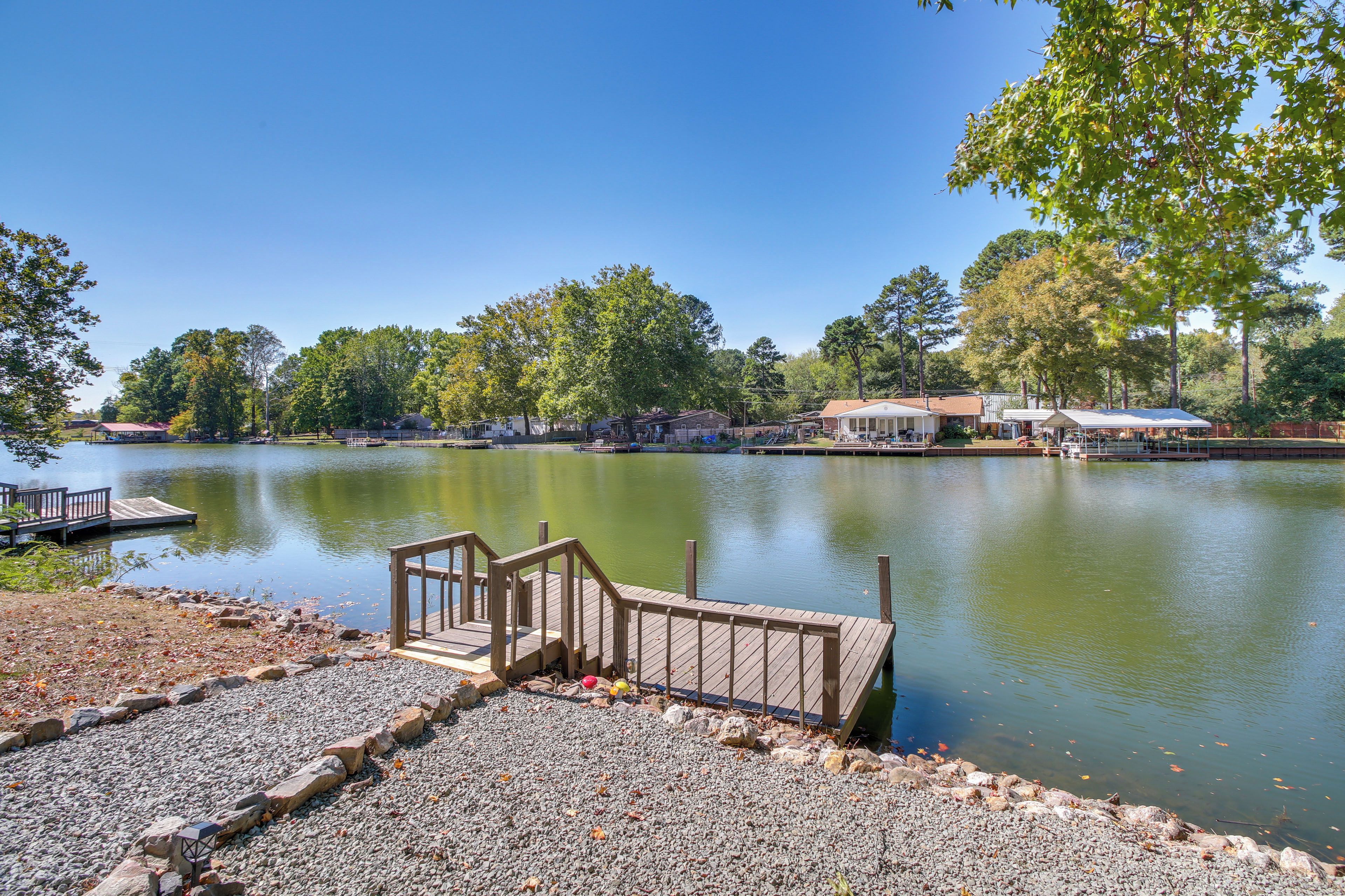 A lakeside dock with a wooden walkway leading to a dock, surrounded by trees and a calm lake.