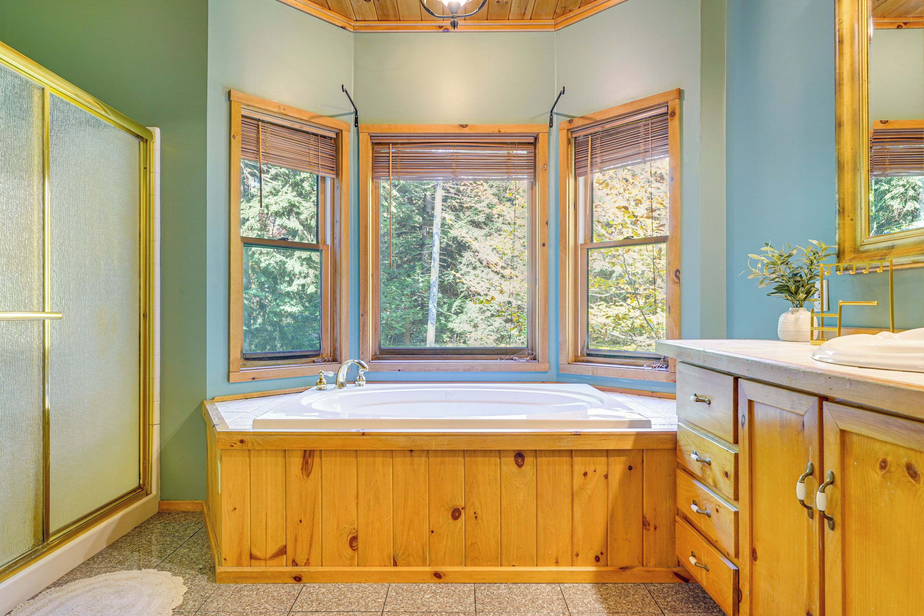 Une salle de bain avec une baignoire en bois, de grandes fenêtres et un lavabo.