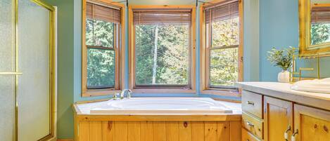A bathroom with a wooden bathtub, large windows, and a sink.