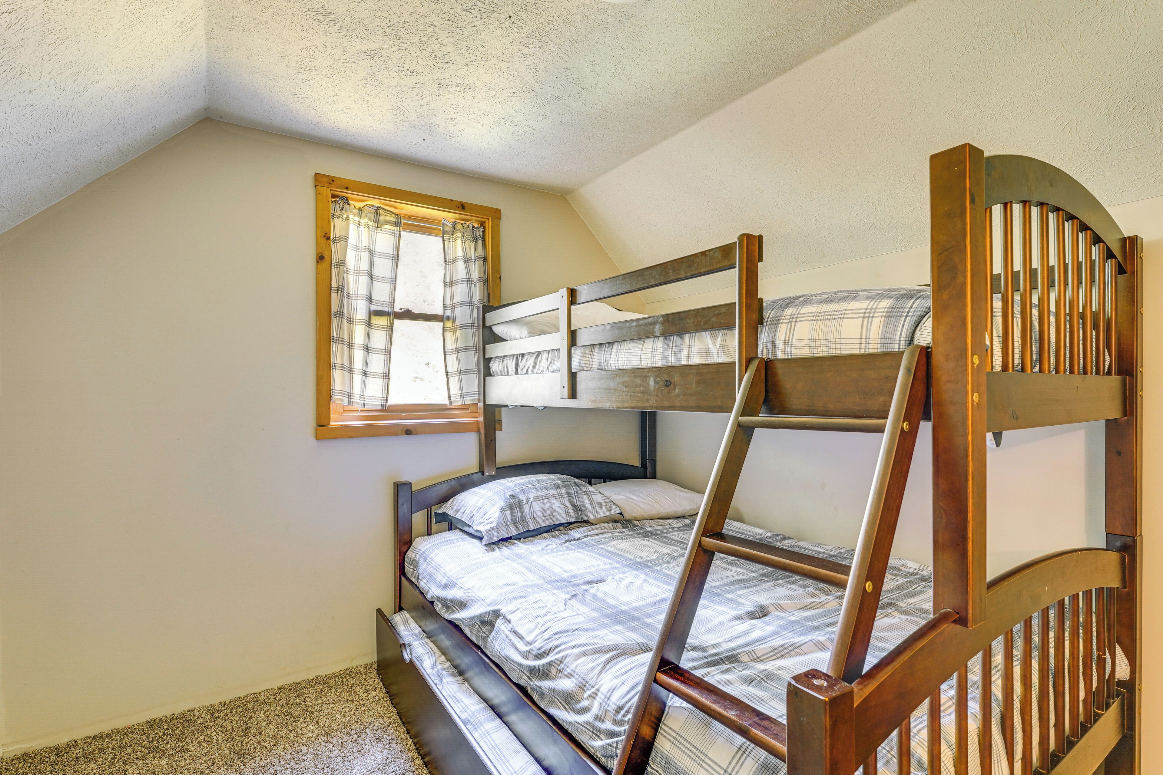 A bunk bed room with a window, wooden ladder, and a plaid bedspread.