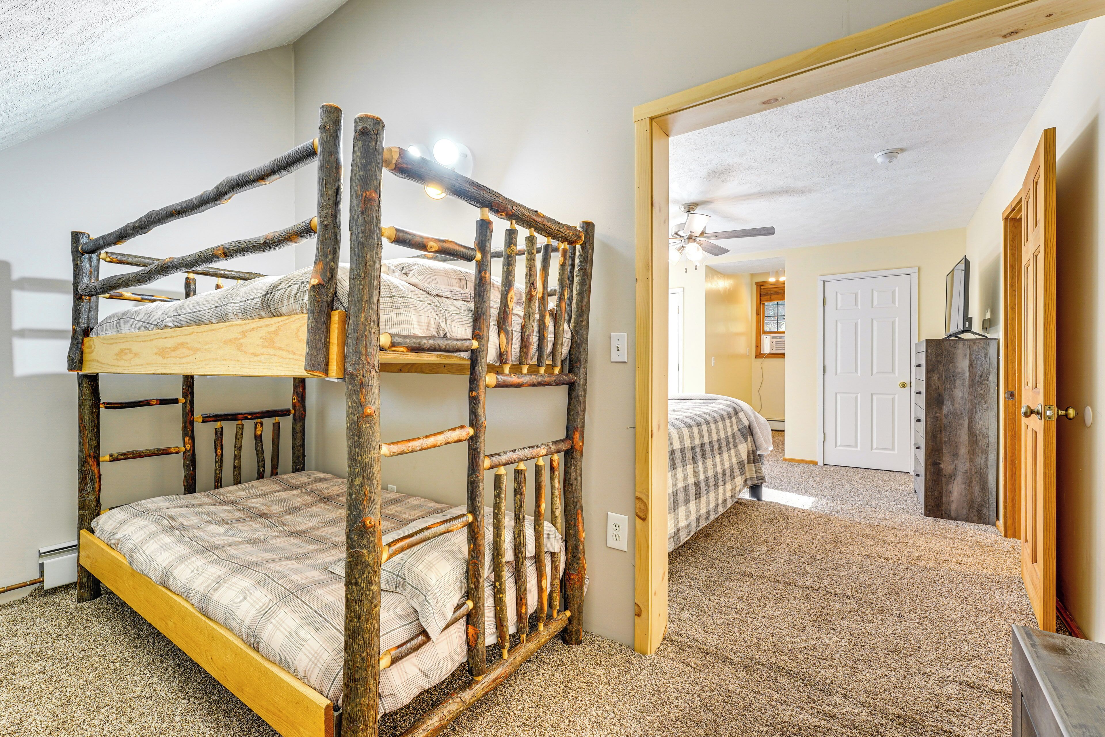 A bunk bed with a rustic design, a carpeted floor, and a door leading to another room.
