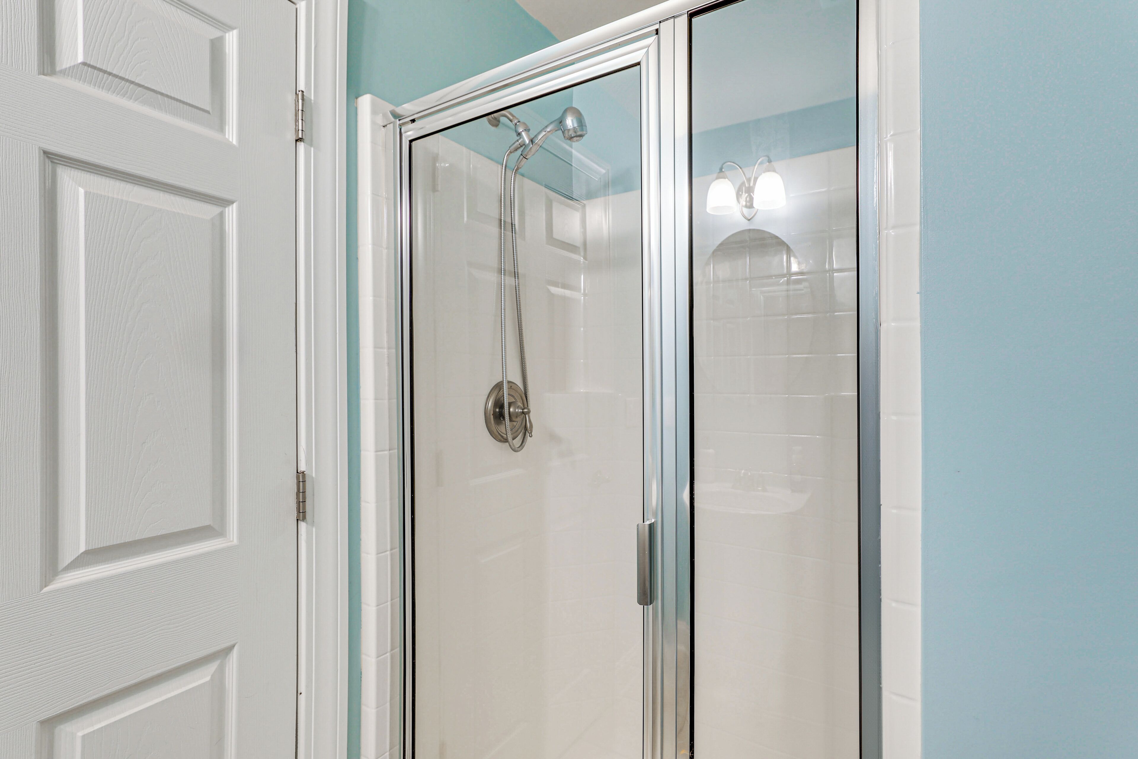 A glass-enclosed shower with a handheld showerhead and a wall-mounted light fixture.