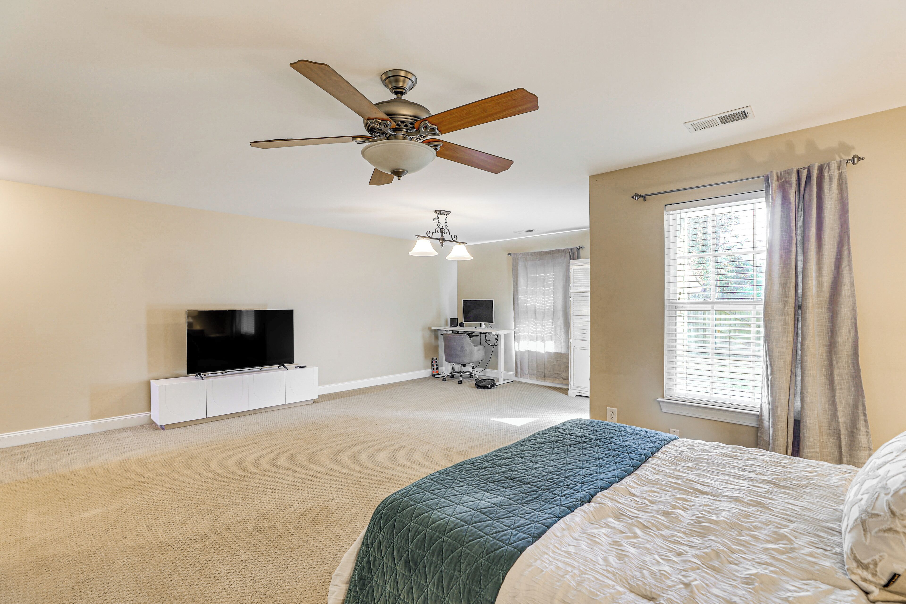 A bedroom with a bed, ceiling fan, TV, and a desk with a computer.