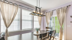 A dining area with a wooden table, chairs, a hanging light fixture, and a view through the window. - Townhome 3 Mi to Wescott Park & Golf Course! (Ladson)