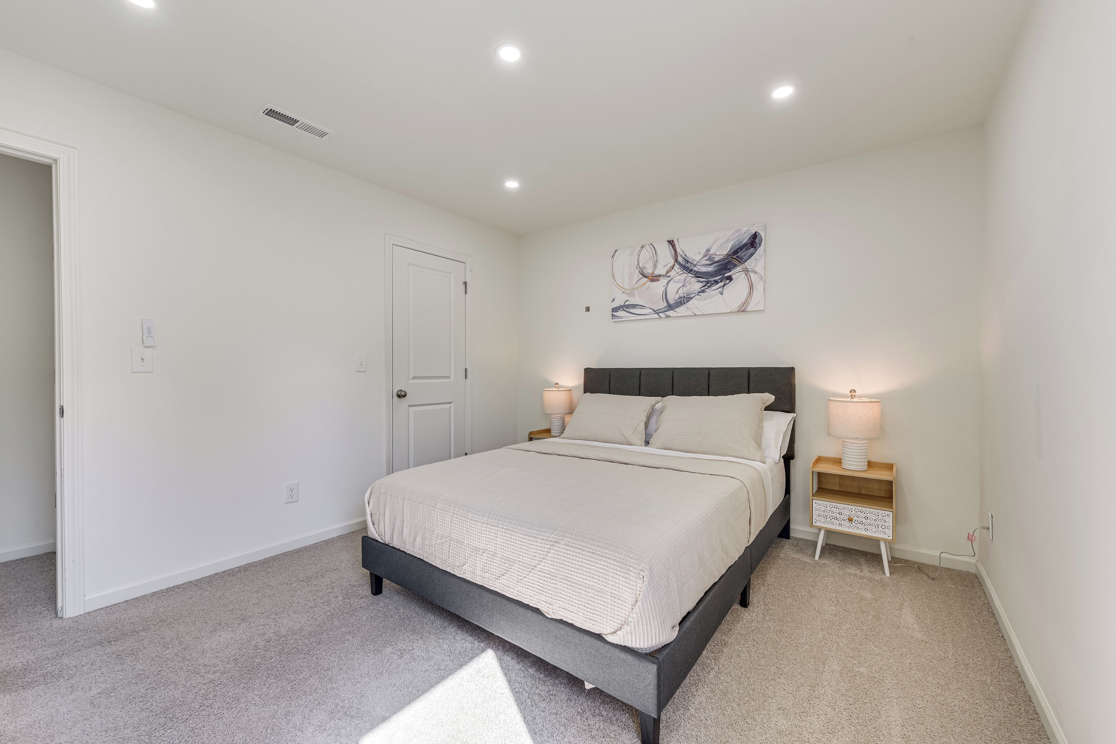 A bedroom with a bed, bedside tables, a door, and a wall-mounted abstract art piece.