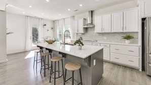 Une cuisine moderne avec des meubles blancs, un grand îlot central doté de tabourets et un réfrigérateur en acier inoxydable.