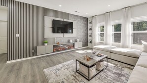 Un salon moderne doté d’un grand téléviseur à écran plat fixé au mur, d’un canapé, d’une table basse et d’une cheminée.