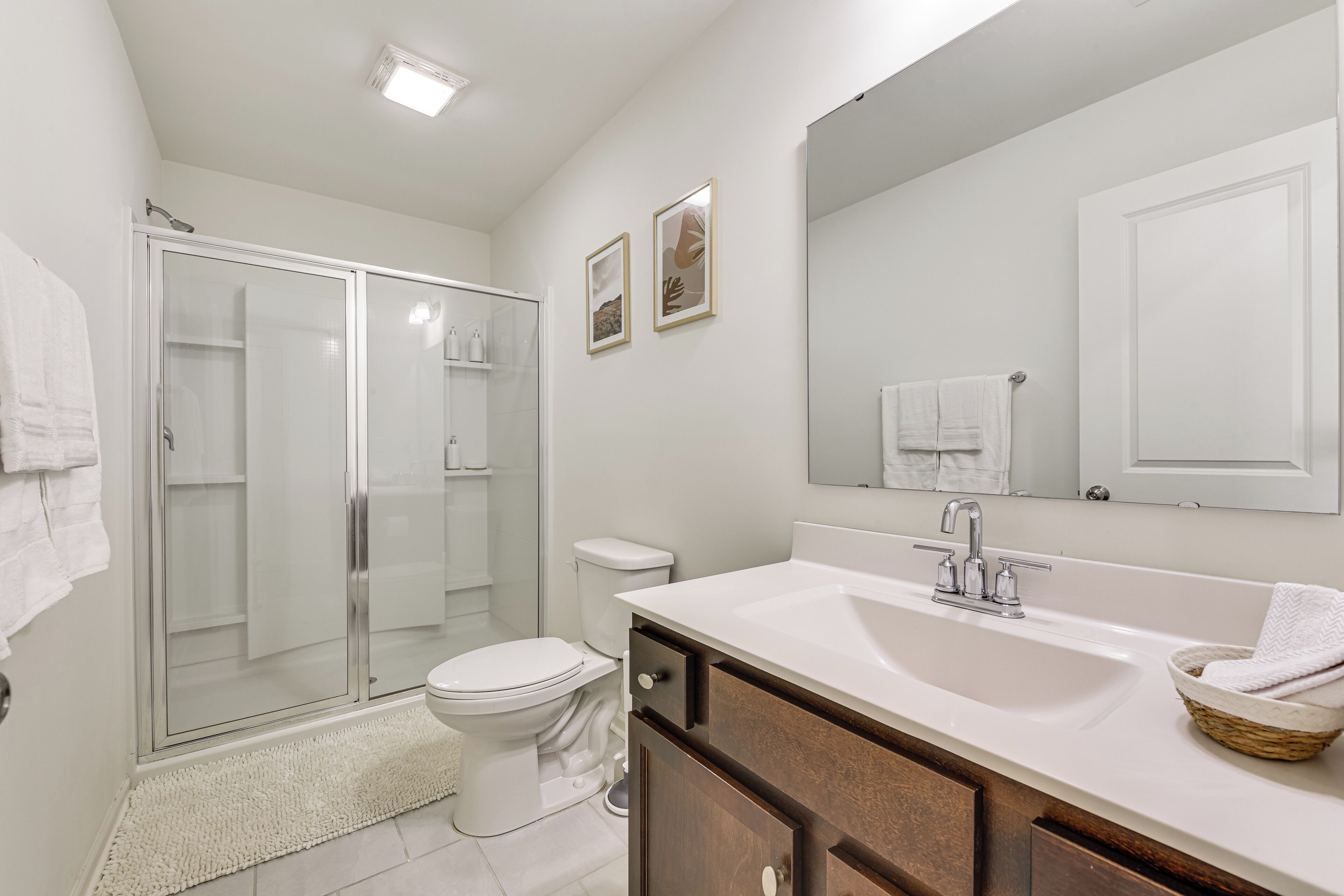 A modern bathroom with a glass shower enclosure, a white toilet, a large mirror, and a white sink with a wooden vanity.
