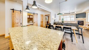 A spacious kitchen with a large granite island, wooden cabinets, and pendant lighting. - Downtown WP Condo w/ Pool: Steps to Concert Venue! (Winter Park)
