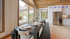 A modern kitchen with white cabinets, a stainless steel refrigerator, and a long dining table set for six.