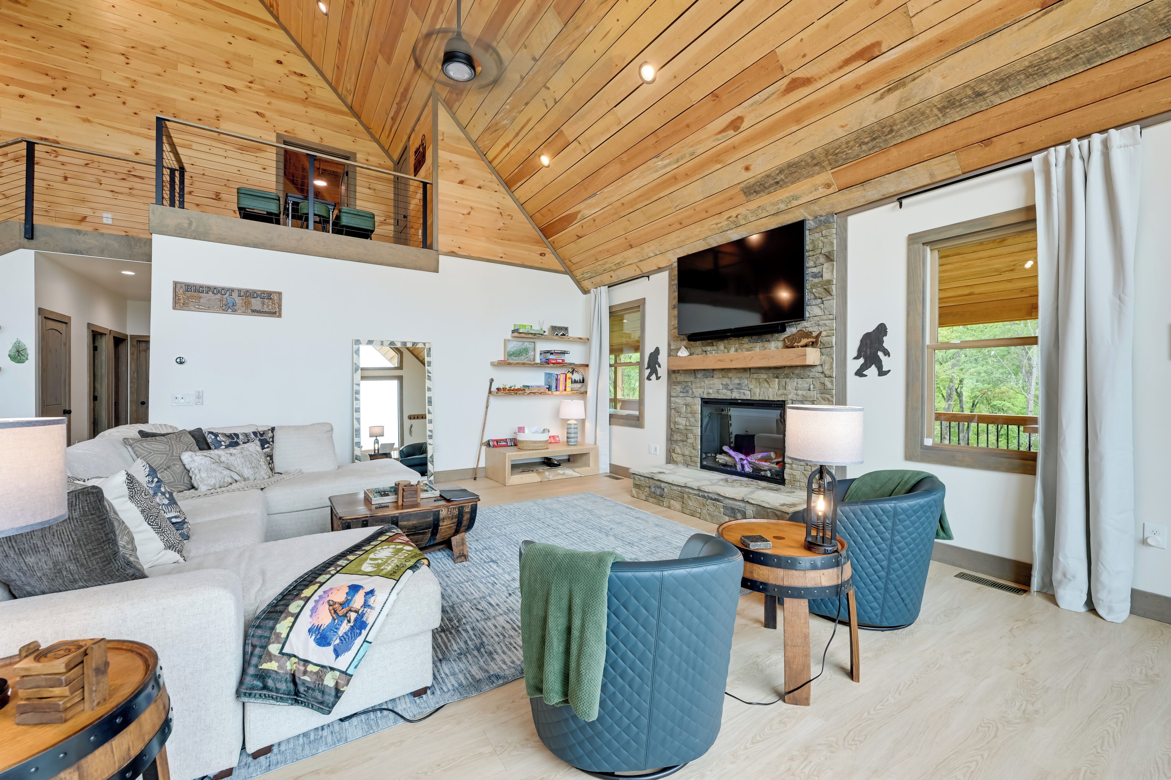 A spacious living area with a high ceiling, a stone fireplace, and a large TV screen.