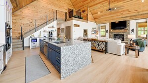 A spacious living area with a kitchen, a dining area, and a fireplace. There is a staircase leading to a loft.